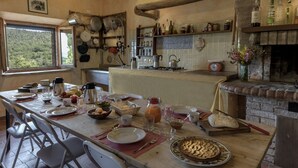 Una cocina rústica con una mesa de madera preparada para el desayuno, una chimenea de piedra y diversos utensilios y electrodomésticos de cocina.