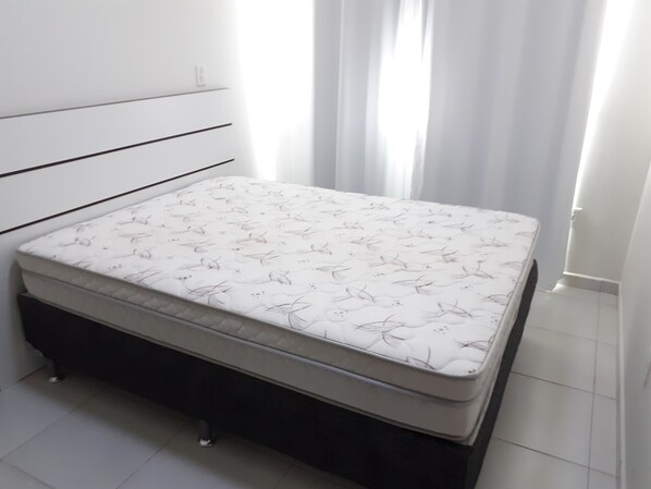 A bed with a floral mattress in a room with white walls and a window with curtains.