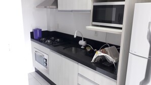 Ett modernt kök med vita skåp, en svart bänkskiva, en spis, en mikrovågsugn och ett kylskåp.