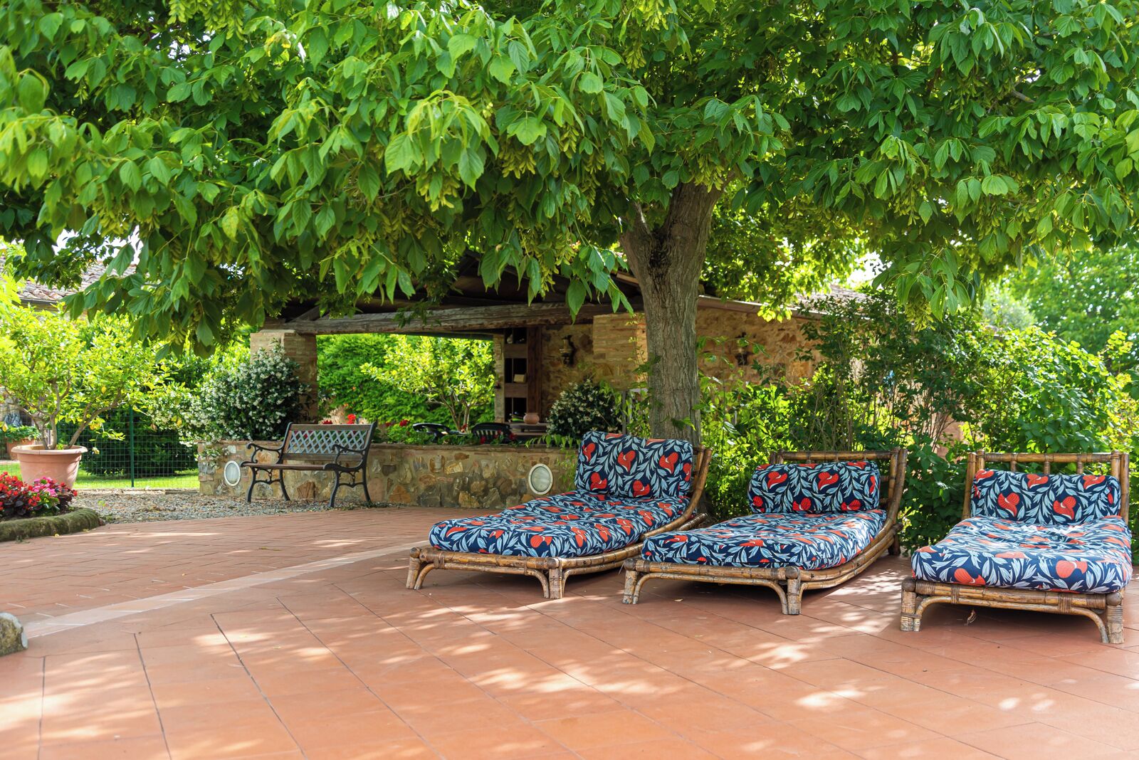 A patio with three wicker lounge chairs and a stone wall in the background.