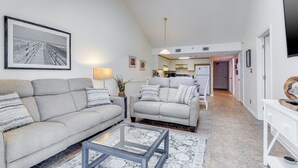 Uma sala de estar moderna com um sofá cinzento, uma mesa de centro de vidro e um espaço de jantar com uma mesa e cadeiras brancas.
