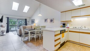 Cozinha moderna com armários brancos, lava-louças e área de jantar com mesa e cadeiras.