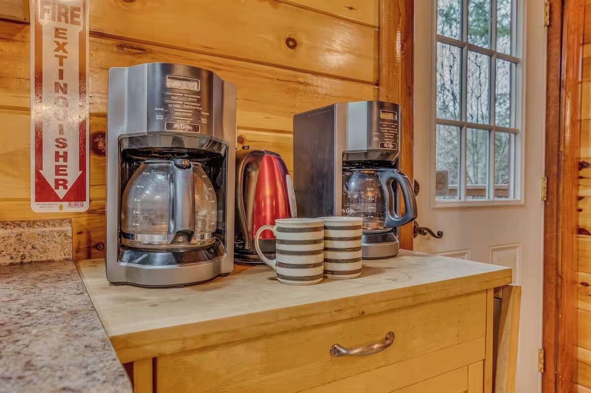 En köksbänk med två kaffebryggare, en röd vattenkokare och två randiga muggar.