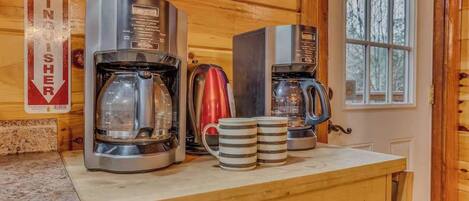 En köksbänk med två kaffebryggare, en röd vattenkokare och två randiga muggar.