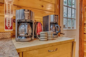 En köksbänk med två kaffebryggare, en röd vattenkokare och två randiga muggar.