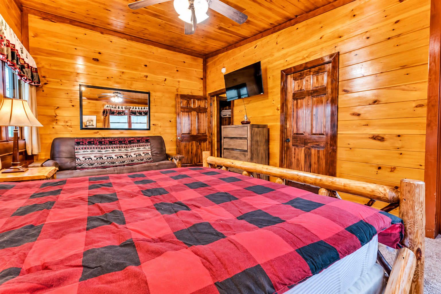 A wooden cabin interior with a large bed, a television, and a fireplace.