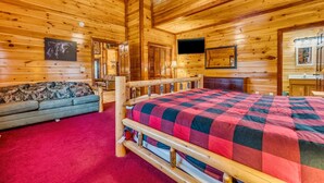 A wooden cabin room with a bed, a sofa, a ceiling fan, and a television. - Heated Pool, Movie Room, Sleeps 30, Dogs Welcome (Cosby)