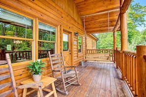 A wooden cabin with a porch, rocking chairs, and a potted plant.