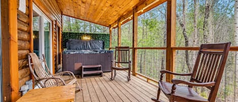 Une terrasse en bois avec un jacuzzi, des sièges et une vue sur la forêt.