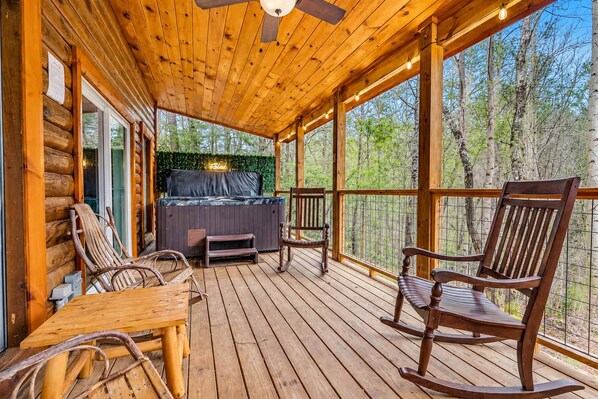 A wooden deck with a hot tub, seating, and a view of the forest.