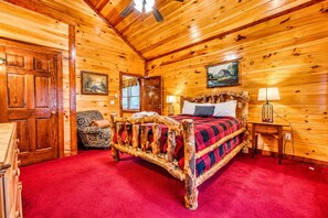 A wooden cabin room with a bed, a chair, and a painting on the wall. - Mountain Retreat • Sleeps29 • Pool • HotTub • Dogs (Cosby)