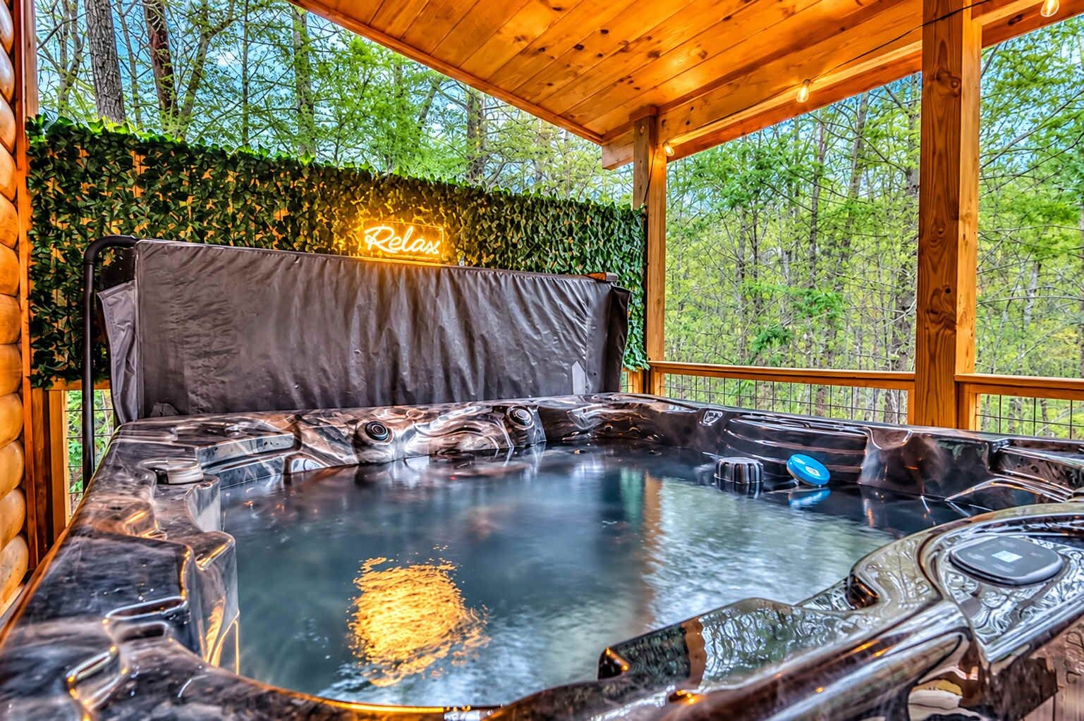 Un jacuzzi con un letrero de neón, rodeado por una terraza de madera y un seto.
