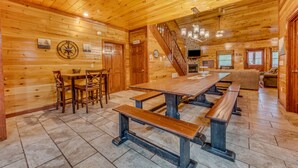 A wooden cabin interior with a dining table, benches, a staircase, and a living area. - Heated Pool, Movie Room, Sleeps 30, Dogs Welcome (Cosby)