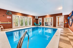 An indoor swimming pool with clear glass walls, a no diving allowed sign, and multiple windows.