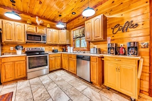 A wooden cabin kitchen with a stove, microwave, and coffee maker.