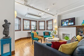 A modern living room with a fireplace, teal chairs, a gray sofa, and a flat-screen TV displaying streaming services.