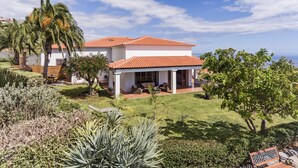 A two-story house with a red-tiled roof, a covered patio, and a well-maintained garden with various plants and a palm tree.