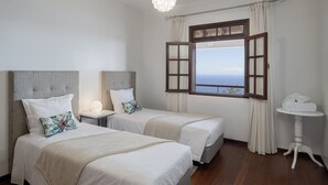 A hotel room with two beds, a window with curtains, a bedside table, and a lamp.