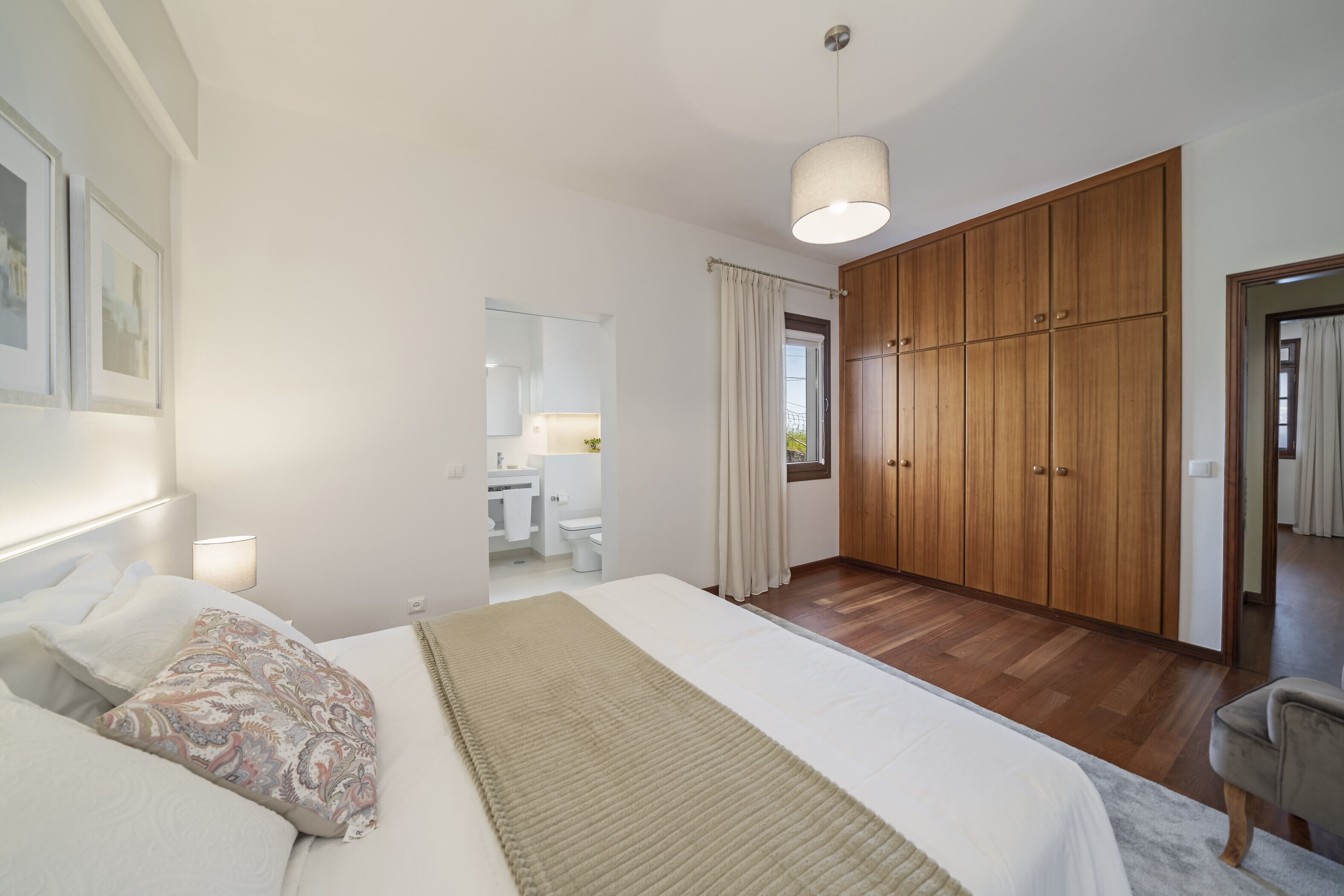 Een slaapkamer met een groot bed, een houten garderobe en een badkamer zichtbaar door een geopende deur.