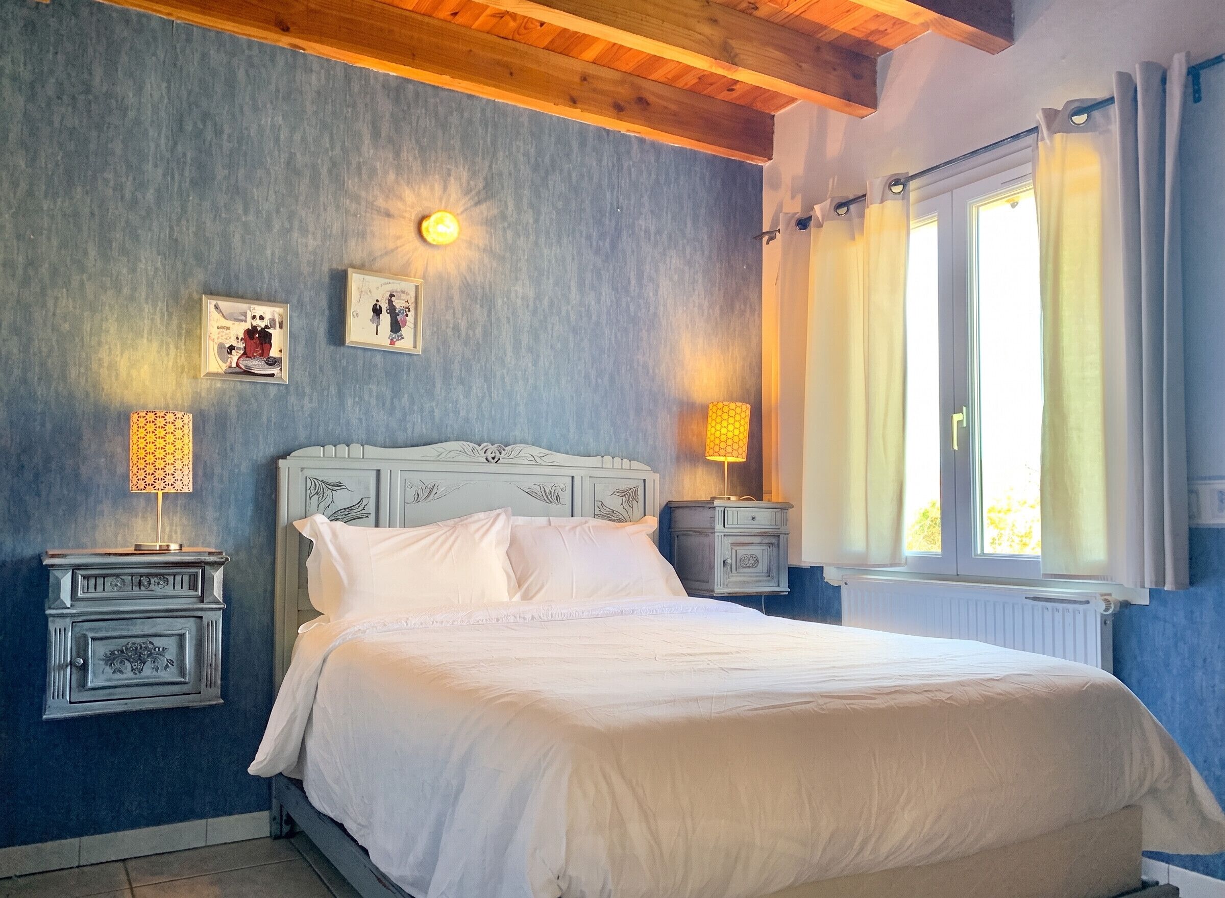 Quarto com cama, duas mesas de cabeceira, relógio na parede e janela com cortinas.
