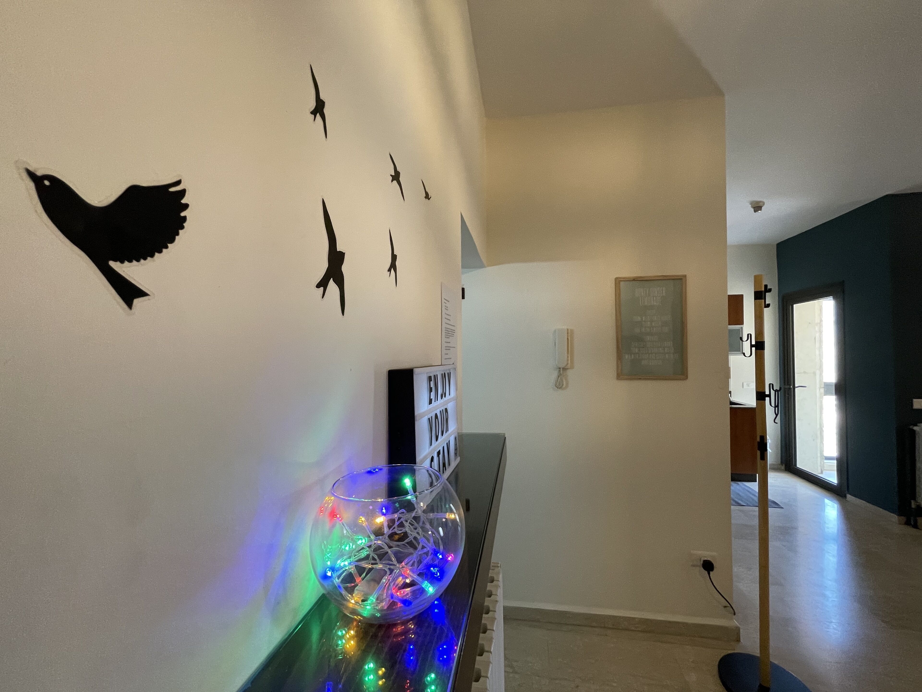 Un passadís amb decoració mural d'ocells, una làmpada decorativa i un cartell emmarcat.