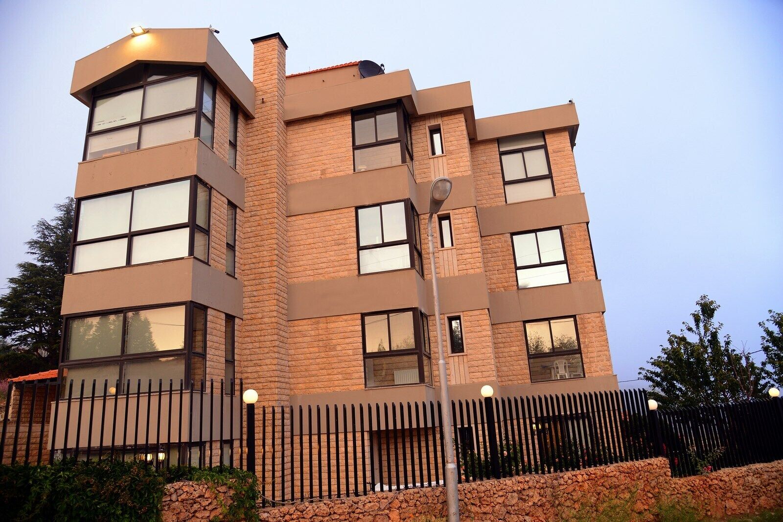 A multi-story building with a brick facade, large windows, and a metal fence.