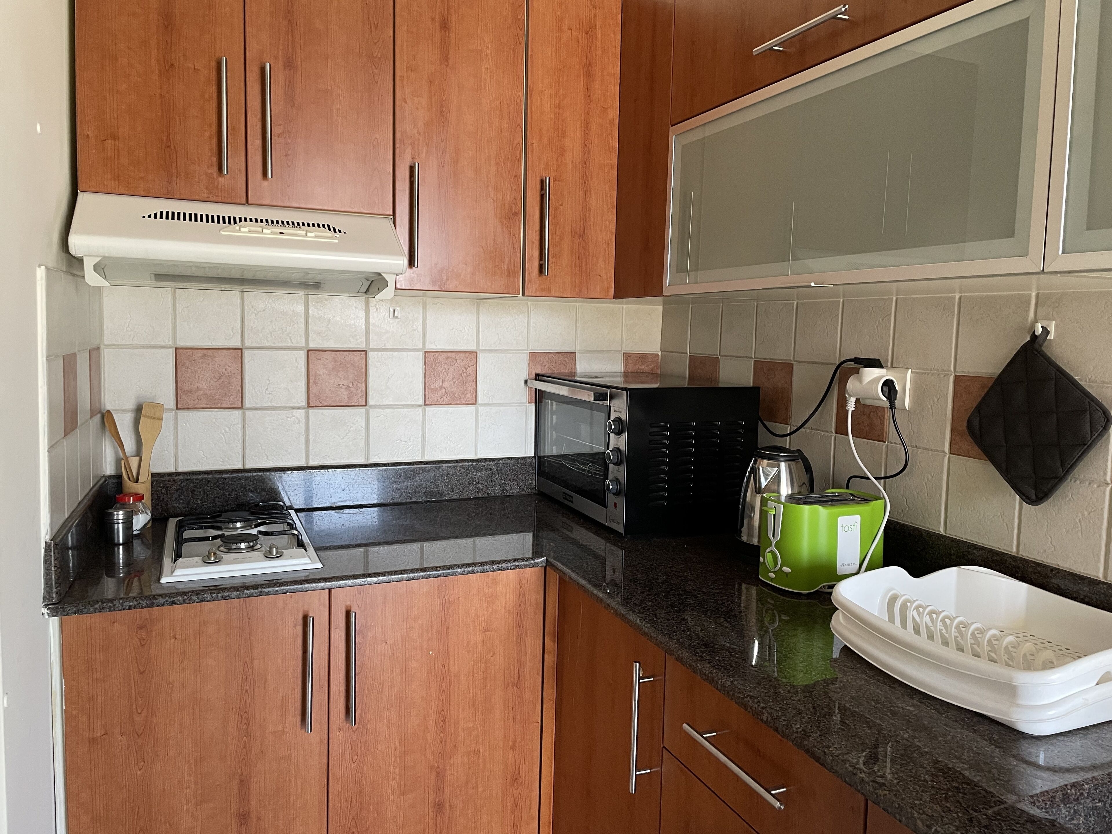 Een keuken met houten kastjes, een gasfornuis, een magnetron, een waterkoker en een groene afwasschaal.