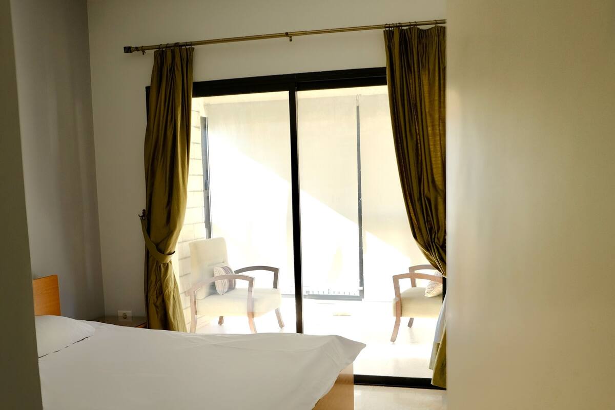 A hotel room with a bed, a chair, and a view of the outside.