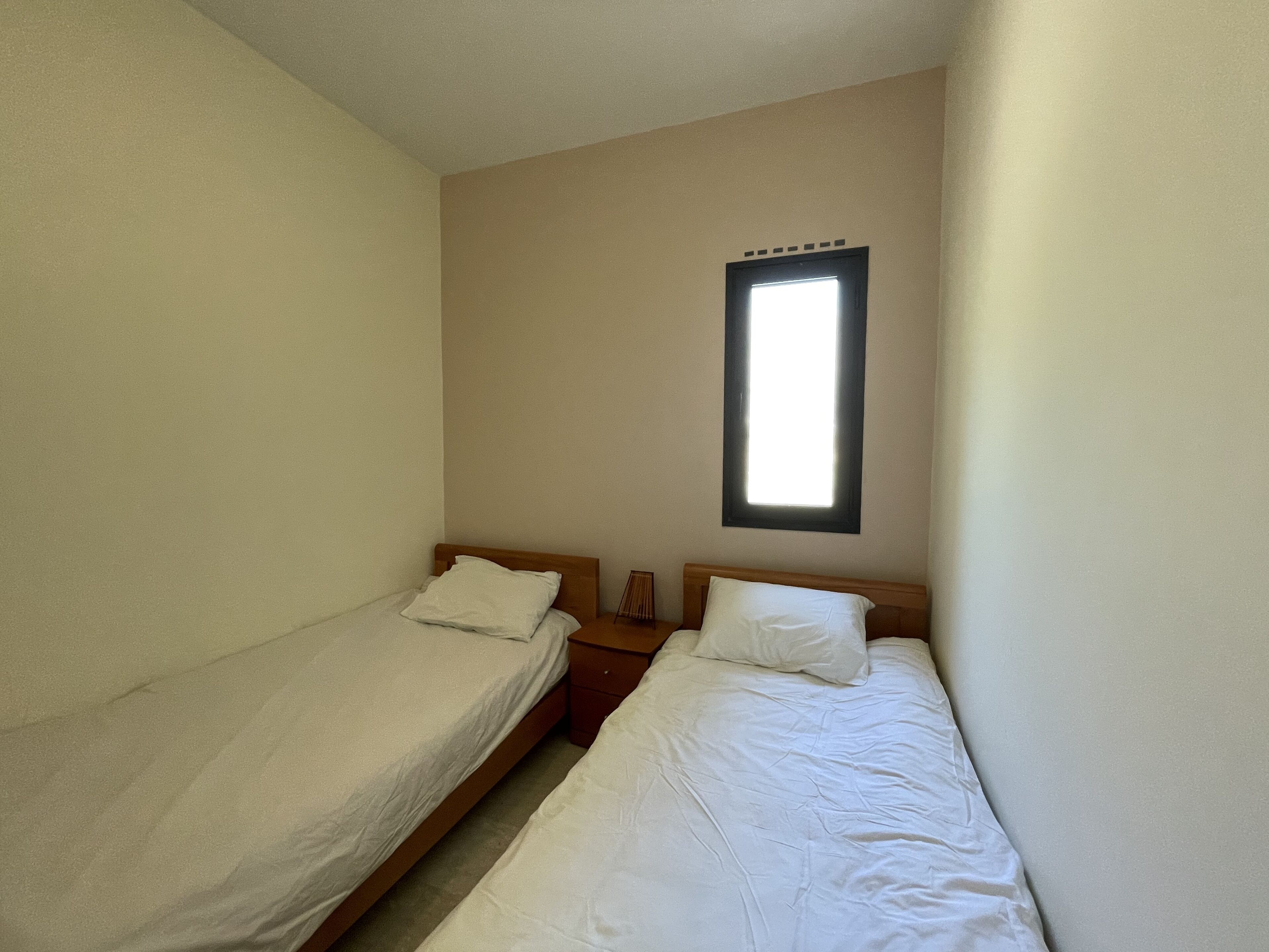 Een kleine, eenvoudige kamer met twee eenpersoonsbedden, een nachtkastje en een raam.