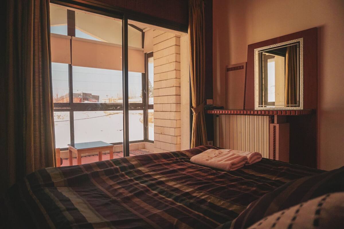 A hotel room with a bed, a window, and a view of the outside.