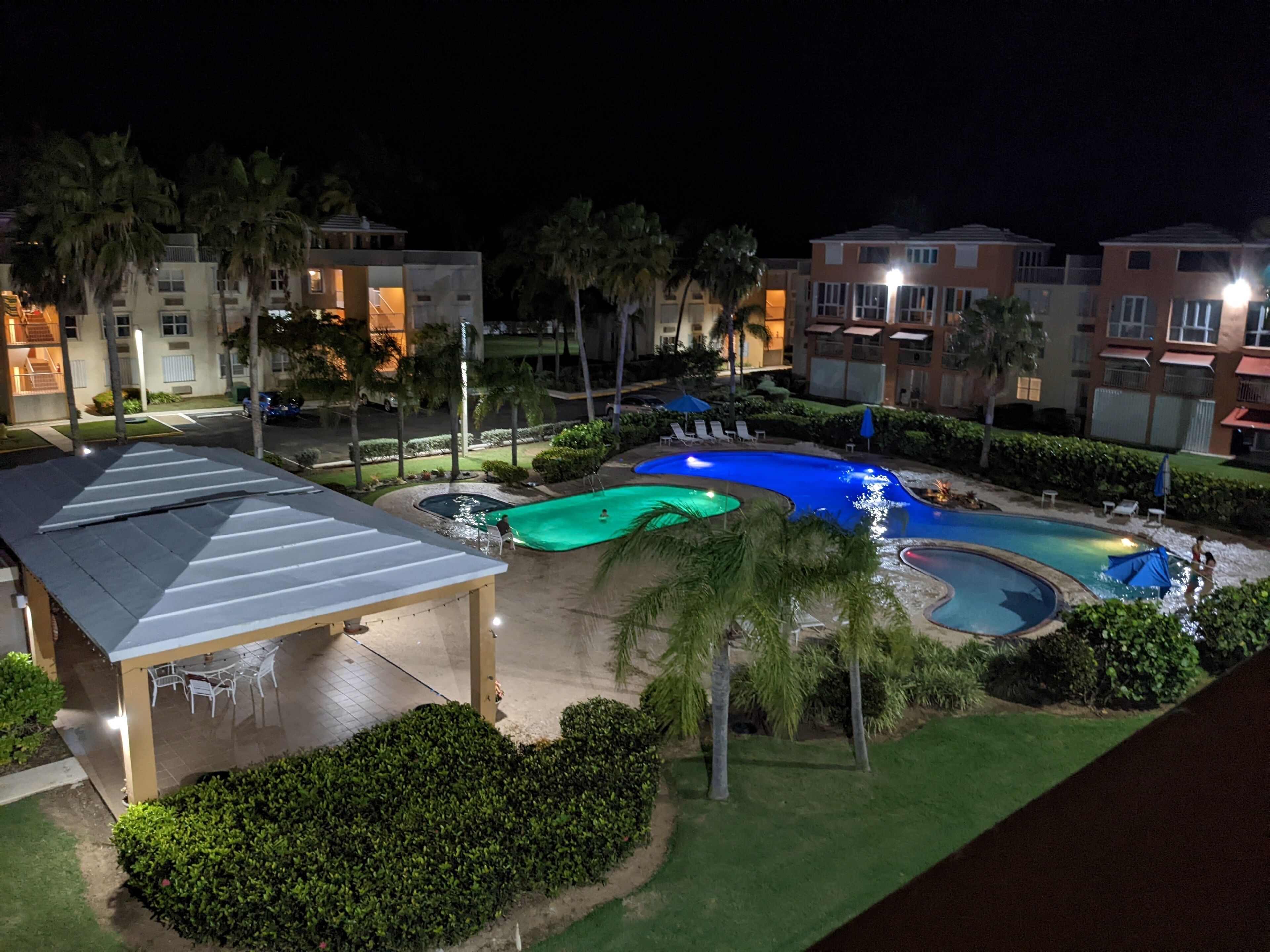 A nighttime view of a resort with multiple swimming pools, a covered patio area, and well-maintained landscaping.
