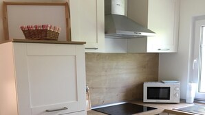Uma cozinha moderna com armários brancos, fogão embutido, micro-ondas e coifa de a ço inoxidável.