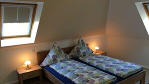 Quarto com cama de madeira, duas mesas de cabeceira com luminárias, janela com persianas e um pequeno clarabóia.