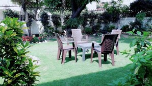 A patio with a table and four chairs, surrounded by lush greenery and a white wall. - Fabulous Large Row House in best location (Chandigarh)