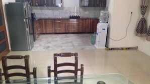 A dining area with a glass table and wooden chairs, a kitchen with marble countertops and wooden cabinets, and a refrigerator. - Fabulous Large Row House in best location (Chandigarh)