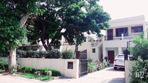 A residential building with a gated entrance, a car parked in front, and a tree-lined driveway. - Fabulous Large Row House in best location (Chandigarh)
