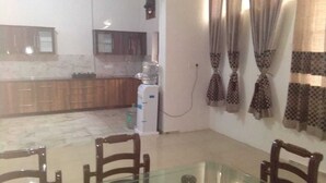 A kitchen with wooden cabinets, a marble countertop, and a water dispenser. There is a dining table with chairs in the foreground. - Fabulous Large Row House in best location (Chandigarh)
