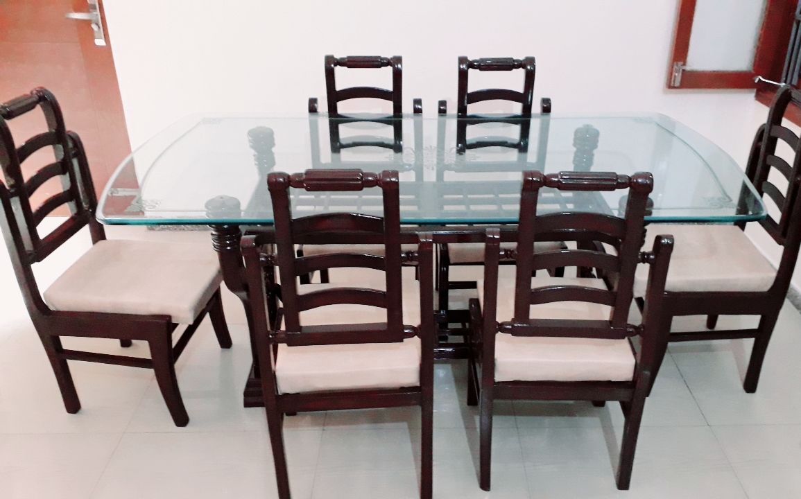 A round glass table surrounded by six wooden chairs with cushioned seats.