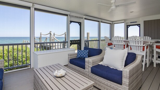 A covered outdoor seating area with wicker furniture, a table, and a view of the ocean. - *Oceanfront Beach Home* (Sandwich)