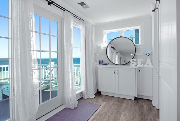 Ein Zimmer mit großen Fenstern, einem runden Spiegel und Blick aufs Meer.