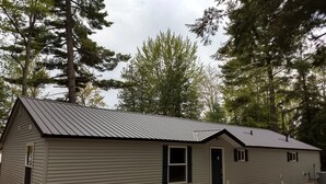 A small, single-story building with a metal roof, surrounded by trees. - Sunken Lake Cottage, w/ 2 Kayaks, Paddle Boat and Canoe (Posen)