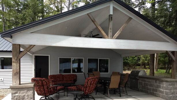 A covered patio with a dining table and chairs, a grill, and a view of the surrounding forest. - Sunken Lake Cottage, w/ 2 Kayaks, Paddle Boat and Canoe (Posen)