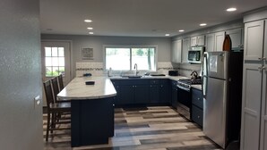 A modern kitchen with a central island, dark cabinetry, stainless steel appliances, and a large window providing natural light. - Sunken Lake Cottage, w/ 2 Kayaks, Paddle Boat and Canoe (Posen)