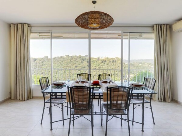 A dining area with a table set for six, large windows offering a view of a forested landscape, and a woven ceiling light fixture.