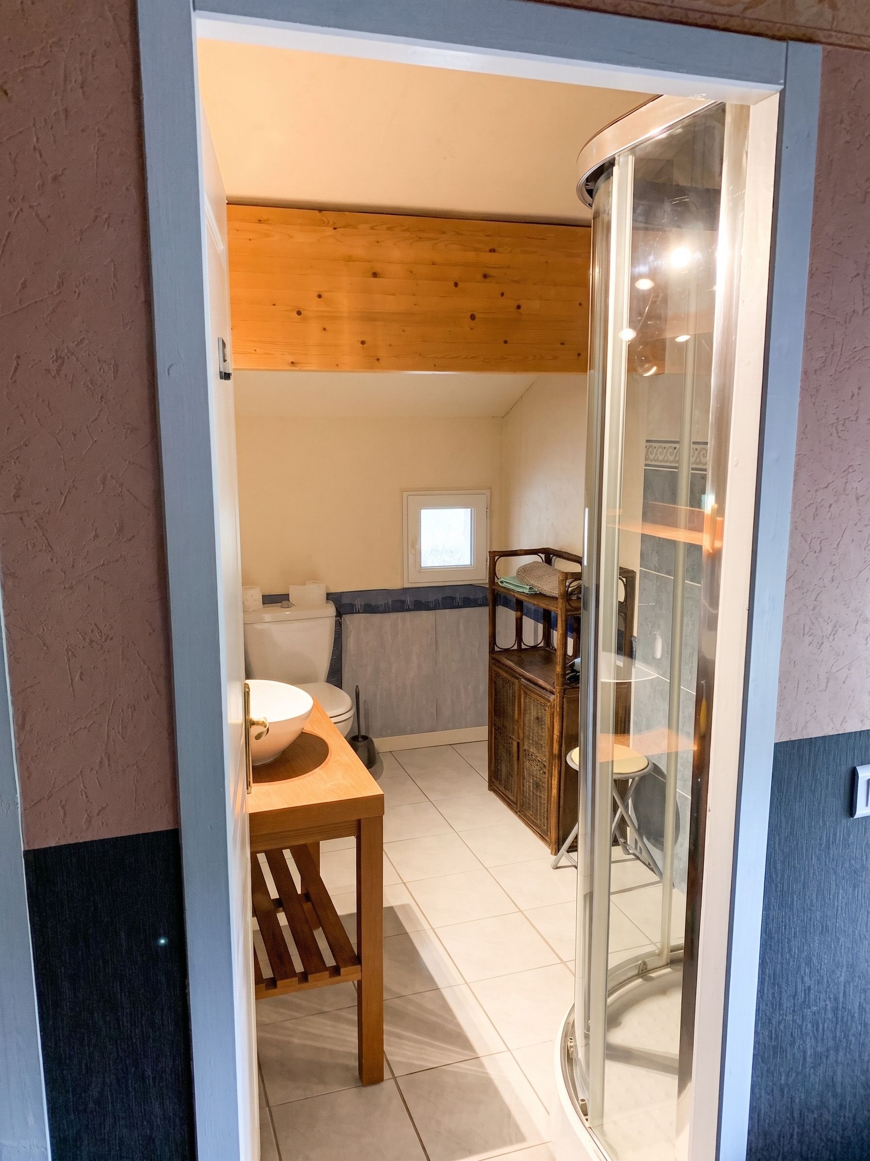 A modern interior with a wooden ceiling, a glass partition, a white toilet, and a dining area with a table and chairs.