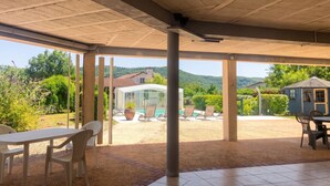 An outdoor patio with a covered area, a table with chairs, a pool, and a view of a house and hills. - Homerez - House in Saint-Géry + Pool (Saint-Géry)
