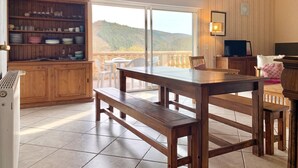 A wooden interior with a dining area, a kitchen with shelves, and a balcony with a view. - Homerez - House in Saint-Géry + Pool (Saint-Géry)