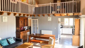 A spacious living area with a wooden dining table, a sofa, and a kitchen in the background. - Homerez - House in Saint-Géry + Pool (Saint-Géry)