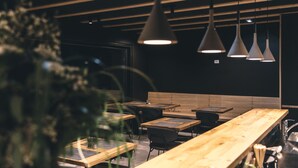 A modern restaurant interior with wooden tables and chairs, pendant lighting, and a black wall. - Hotel Majer'ca (Bohinj)