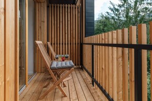 A wooden deck with a cushioned chair and a small table, a black metal railing, and a glass door leading to the interior. - Hotel Majer'ca (Bohinj)